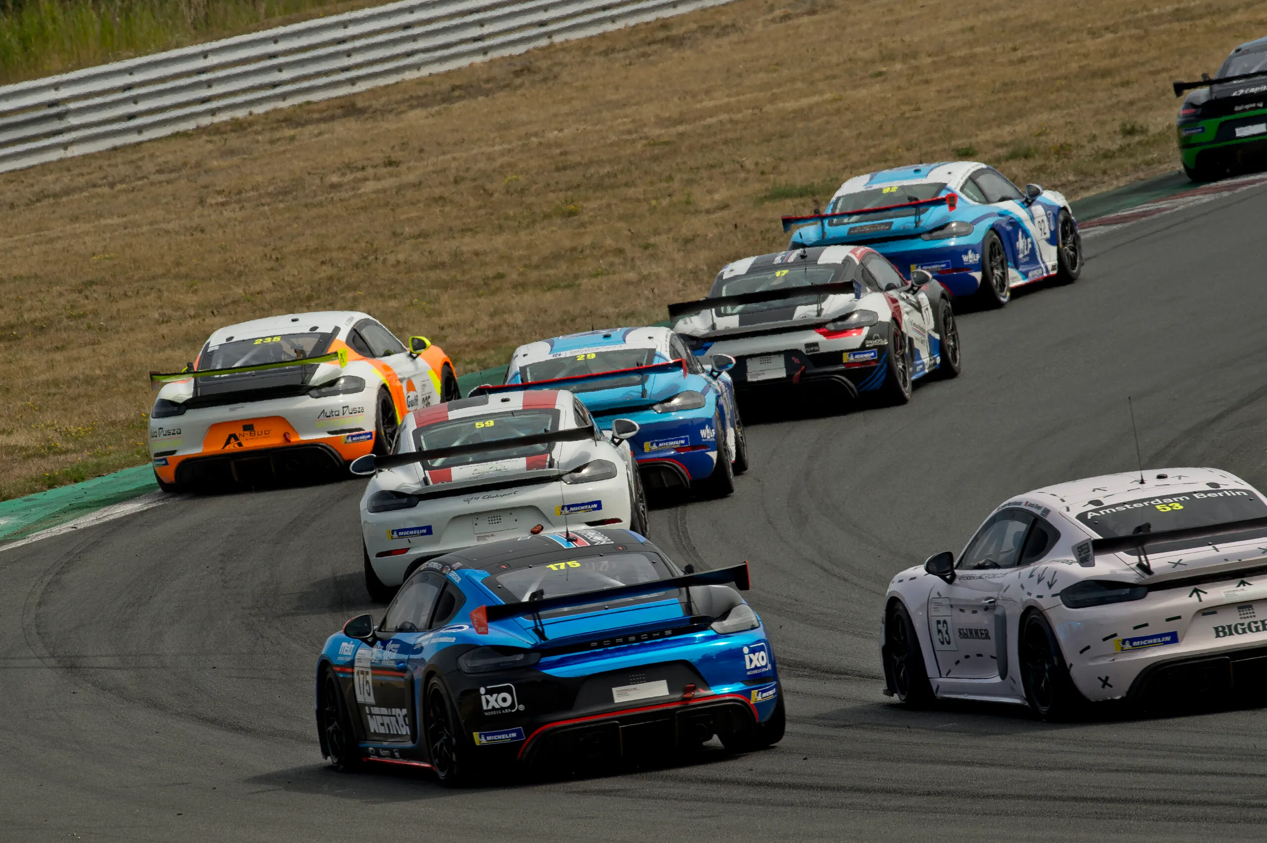 Stawka wyścigowych Porsche Cayman GT4 w zakręcie, wśród nich auto Auto Dusza Motorsport